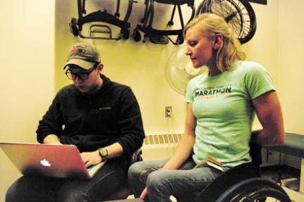 A woman in a wheelchair looking at a laptop screen being used by a lab researcher